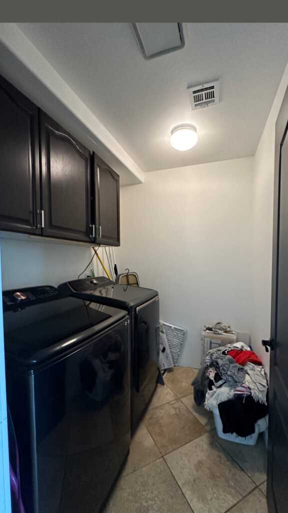 The Before picture of a laundry room with white walls, dark brown stained cabinets on the walls hanging about the washer and dryer.