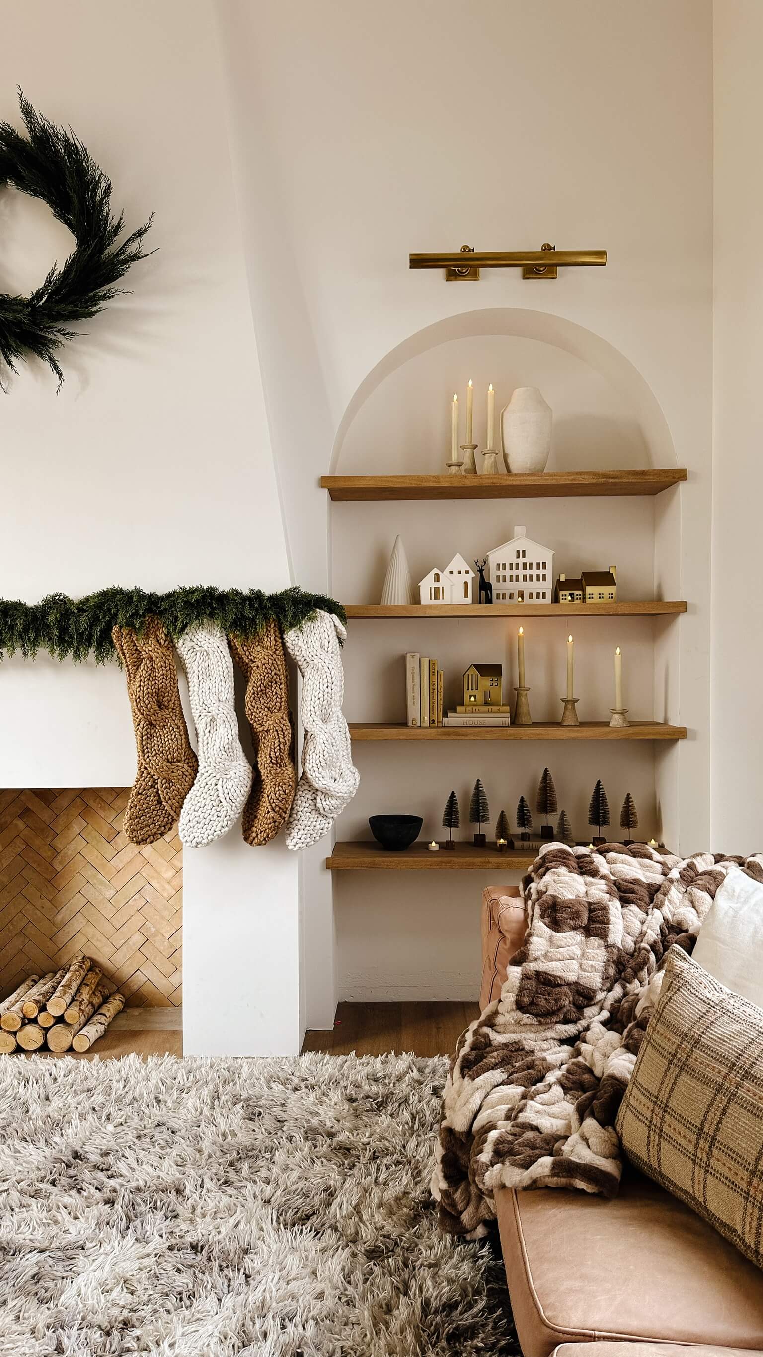 A front room featuring a fireplace and arch with floating shelves all decorated for Christmas in neutral colors.