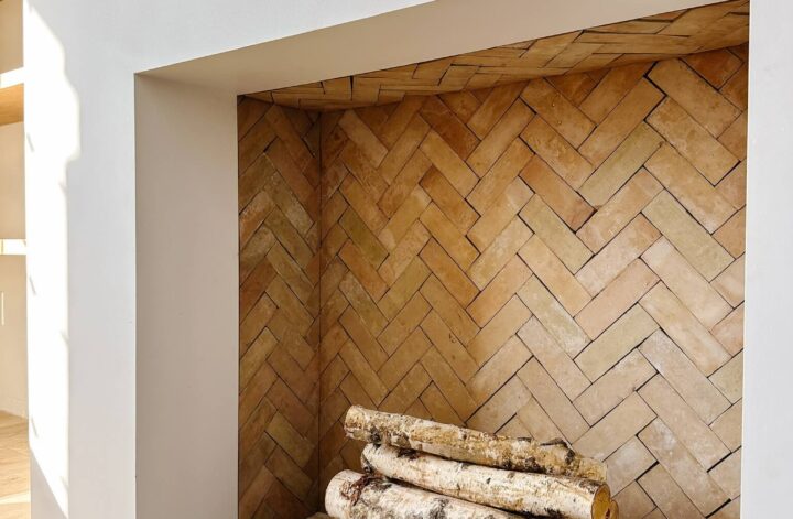 A fireplace with tile in a herringbone pattern a small pile of logs sitting in the center.