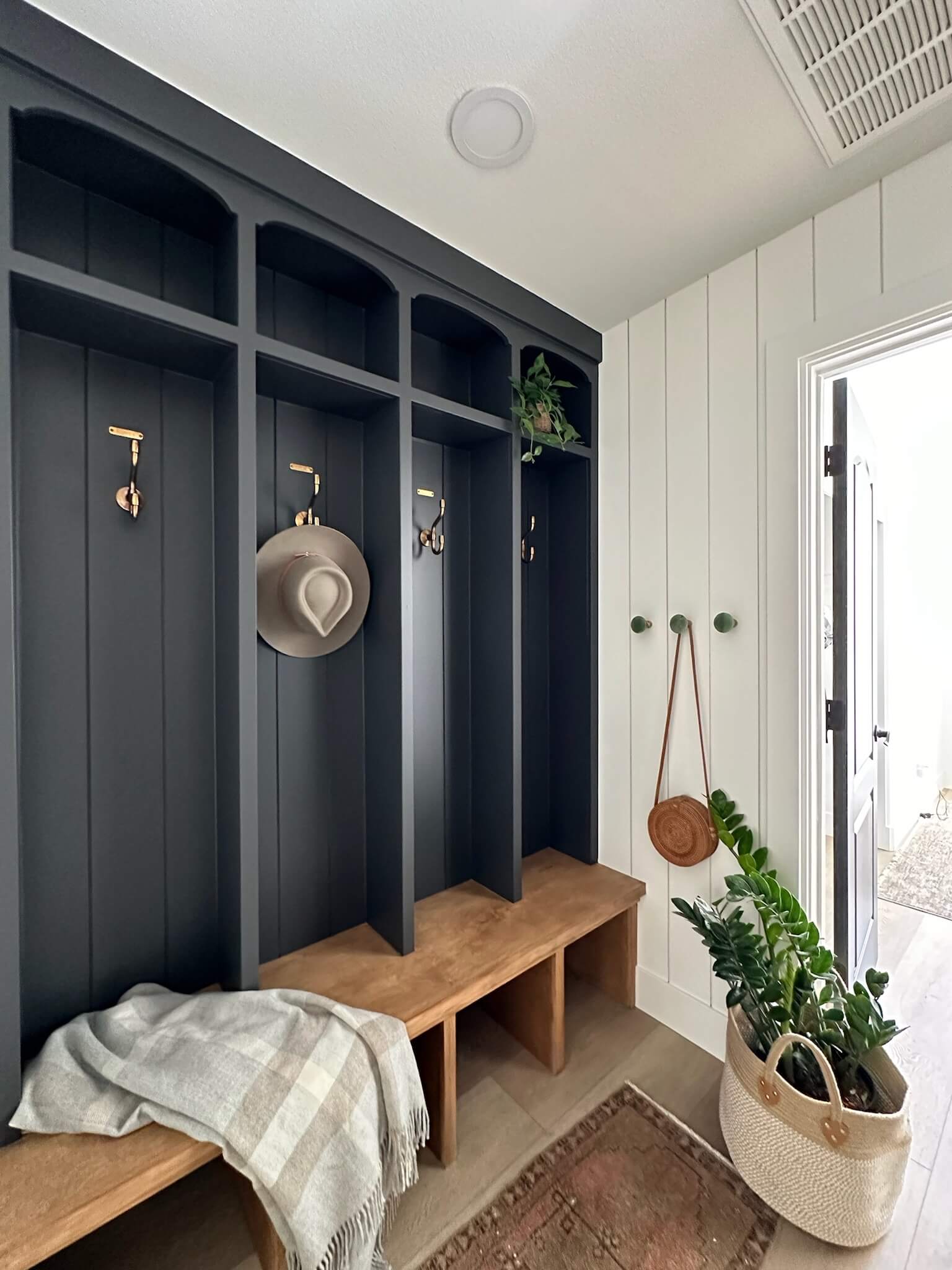 Newly renovated mud room with dark blue lockers and a stained wooden bench underneath.