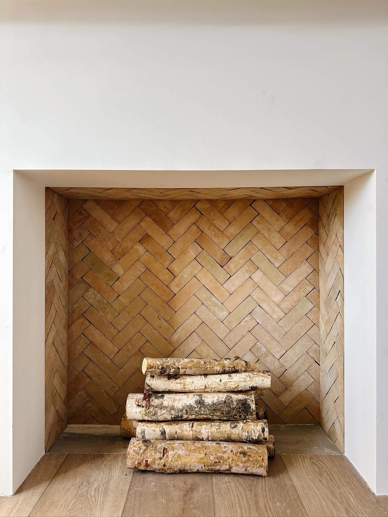 A neutral themed tiled fireplace in a herringbone pattern.