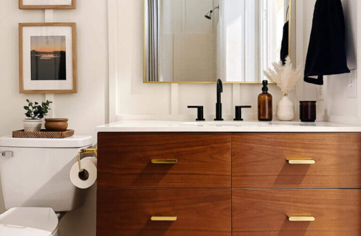 Brown bathroom vanity with gold hardware and a gold framed arched mirror to match featured in a newly renovated guest bathroom.