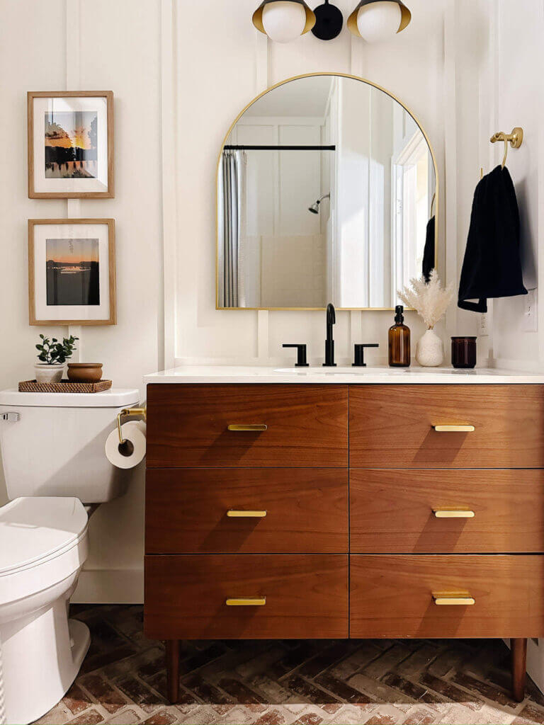 Brown bathroom vanity with gold hardware and a gold framed arched mirror to match featured in a newly renovated guest bathroom.